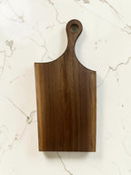 24 inch walnut live edge charcuterie  handle board on a white marble surface.