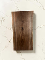 24 iinch walnut wood  live edge board  displayed vertically on a light beige marble surface.