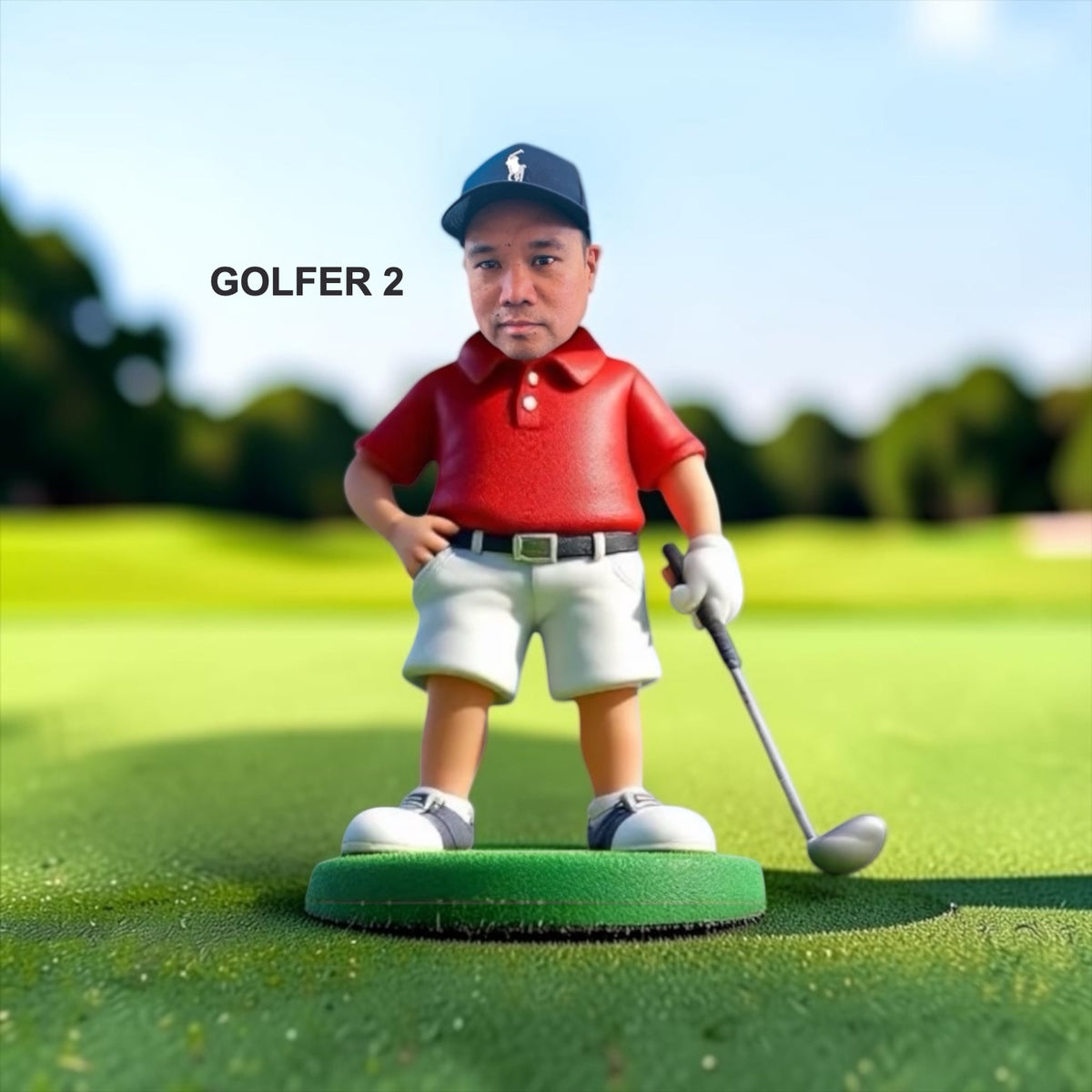 A golfer stands on a green circular base on a golf course. The golfer wears a navy cap with a white logo, a red polo shirt, white shorts, and white shoes, and holds a golf club down. Style Golfer 2.