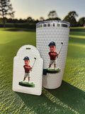 A custom printed golf-themed tumbler and matching tee holder set, featuring a golf ball-dimpled white design a with a golfer in a red shirt and navy cap, displayed on a green golf course background. 