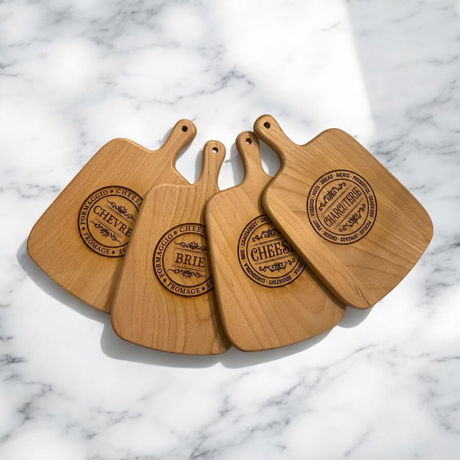 Four wooden serving boards with handles. Each board has a circular laser-engraved logo featuring the words 'CHARCUTERIE','BRIE', ' CHEESE', 'CHEVRE'.