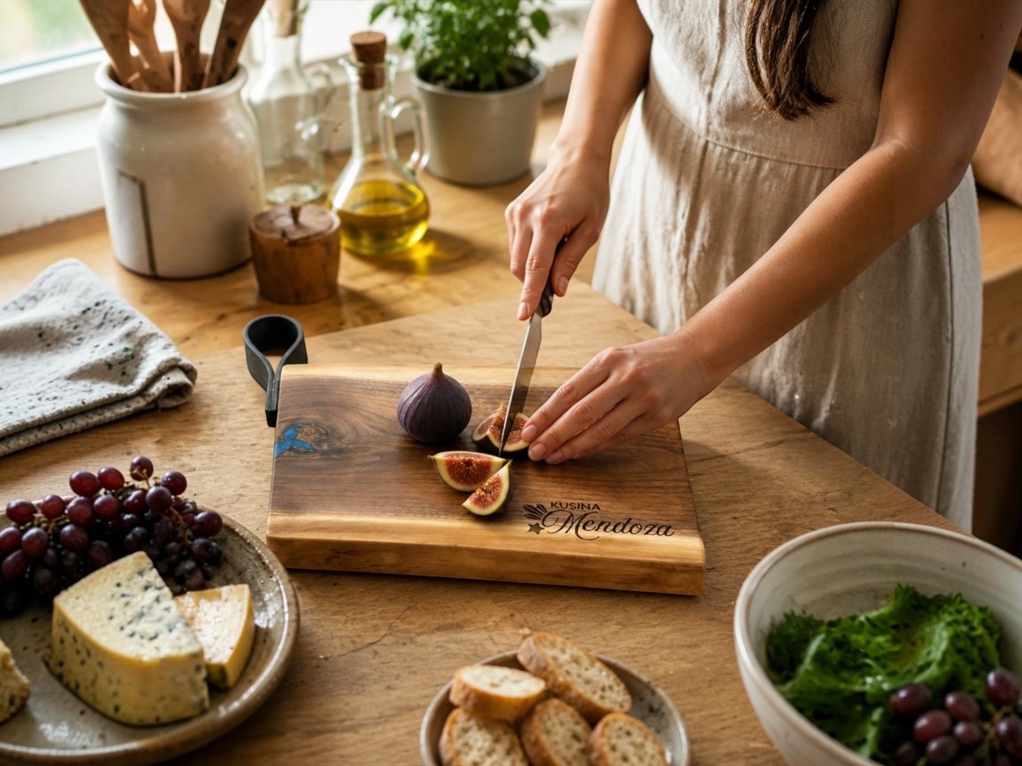 A person in a beige dress slices a fig on a wooden cutting board engraved with 'Mendora', set on a rustic wooden table with cheese, grapes, bread, and a salad nearby.