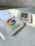 Two square white Google review placeholders on a light gray surface. One shows the colorful Google G logo with the text 'review us on Google' and five stars with NFC icon on the top right hand side, and the other shows a QR code above the Google reviews logo.
