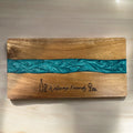 A rectangular wooden serving board with a natural wood grain finish and a horizontal turquoise resin inlay. The board is engraved with the words 'Welcome Friends' in script, flanked by a wine bottle and wine glass icons.