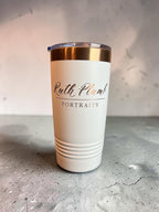 A white insulated travel tumbler with a clear lid and metallic rose gold band, featuring the text 'Ruth Plum Portraits' printed on the front, set on a gray concrete surface.